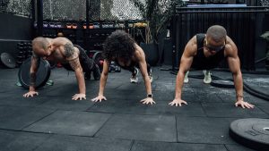 Three individuals performing push-ups together in a Mexico City gym setting.